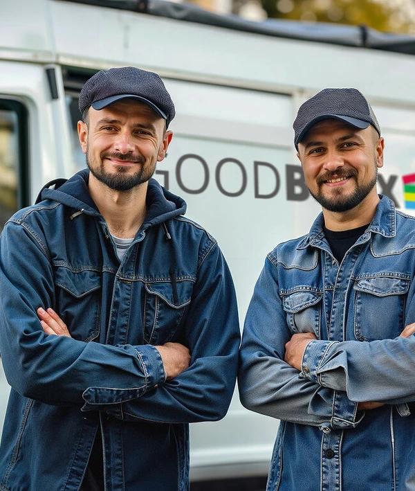 Zwei Männer in Jeansjacken und Mütze stehen mit verschränkten Armen vor einem weißen Van und lächeln.
