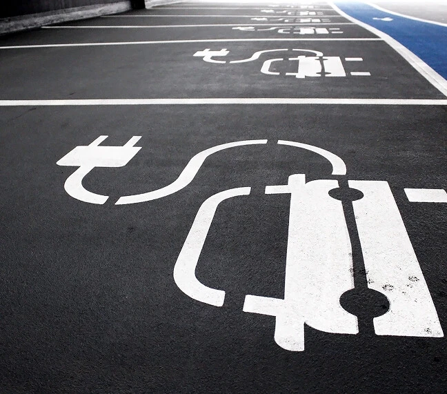 Ein Parkplatz mit gekennzeichneten Bereichen für Elektroautos an dem ein blauer Fußgängerweg verläuft.