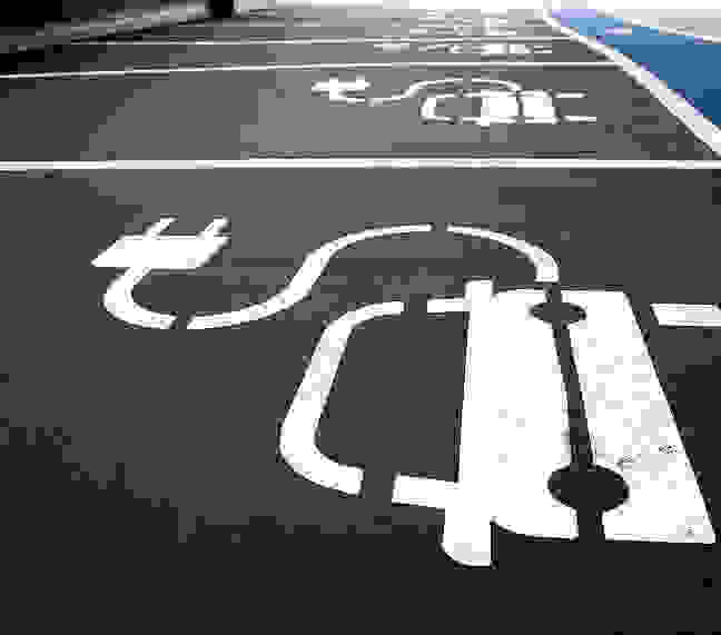 Ein Parkplatz mit gekennzeichneten Bereichen für Elektroautos an dem ein blauer Fußgängerweg verläuft.