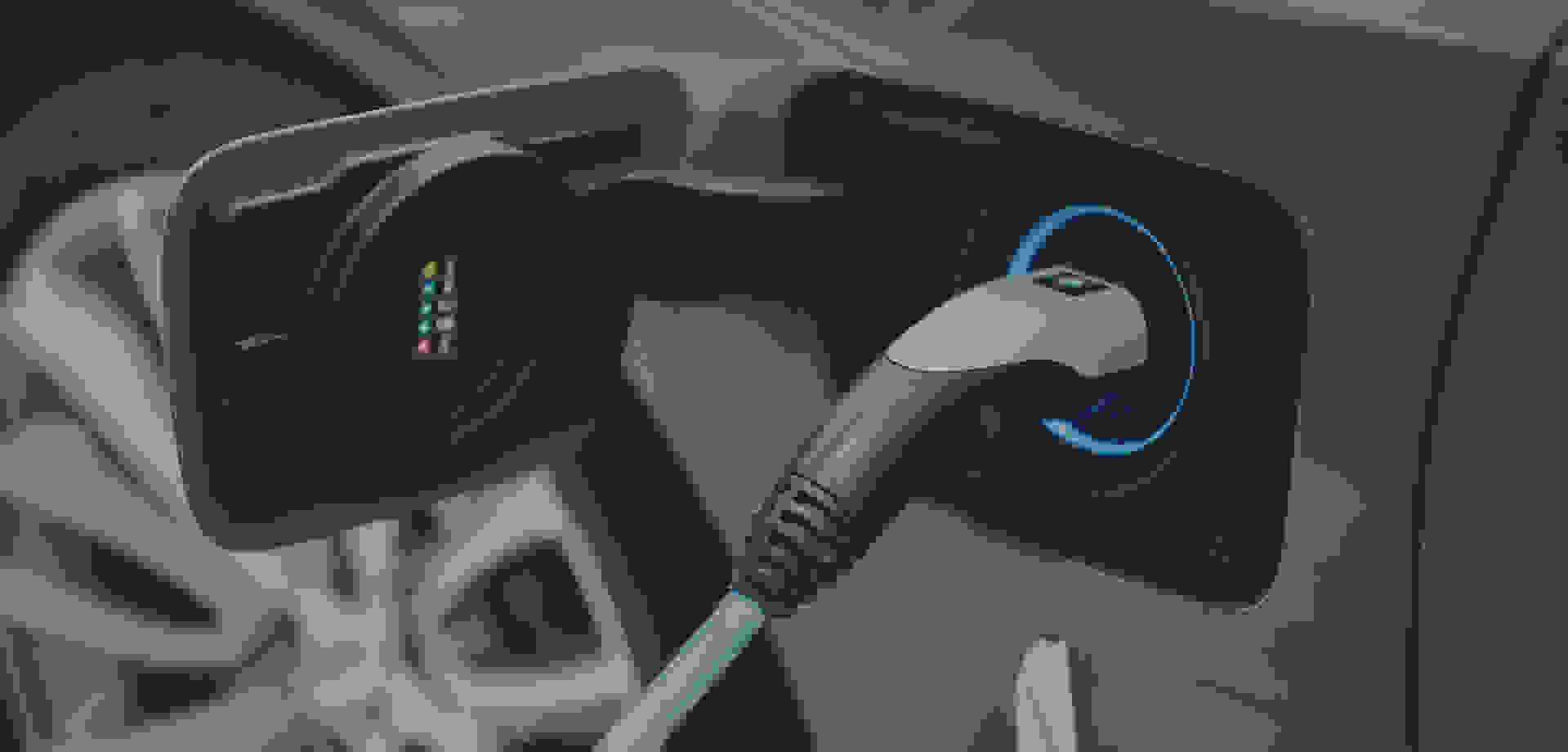 Ein graues Elektroauto steht mit geöffneter Ladeklappe an der Ladesäule, während ein blauer Ring um den Stecker leuchtet.