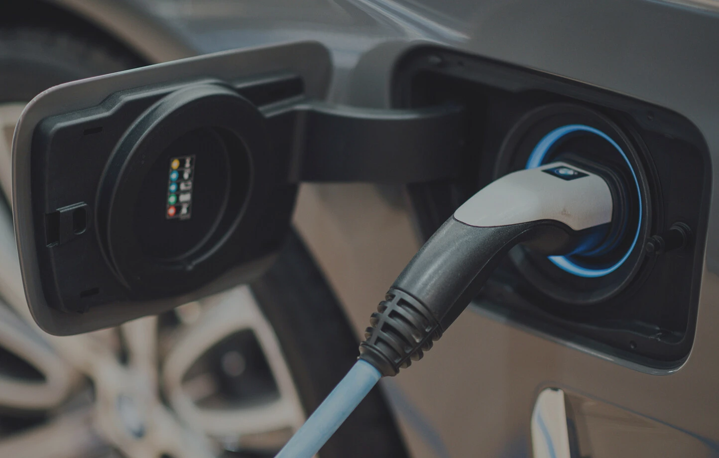 Ein graues Elektroauto steht mit geöffneter Ladeklappe an der Ladesäule, während ein blauer Ring um den Stecker leuchtet.