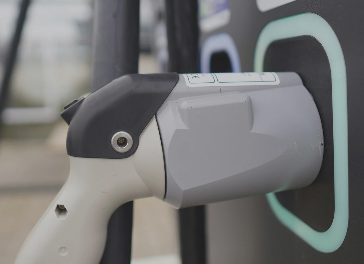 Ein weißes Ladegerät für E-Autos ist an einer grauen Ladestation mit mintfarbener Markierung befestigt – der Hintergrund ist unscharf.